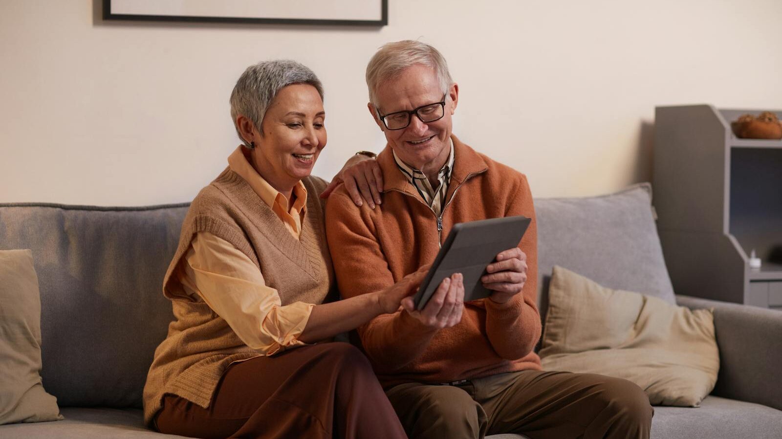 Happy senior couple sitting together on a sofa using a tablet indoors.